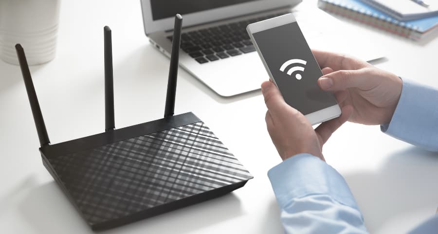 Man holding a mobile device at a desk beside a wireless router.